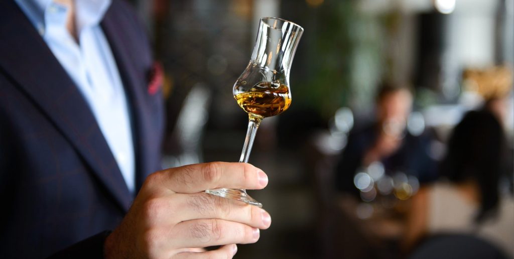 A man in a suit holding up a whiskey tasting glass to assess the color