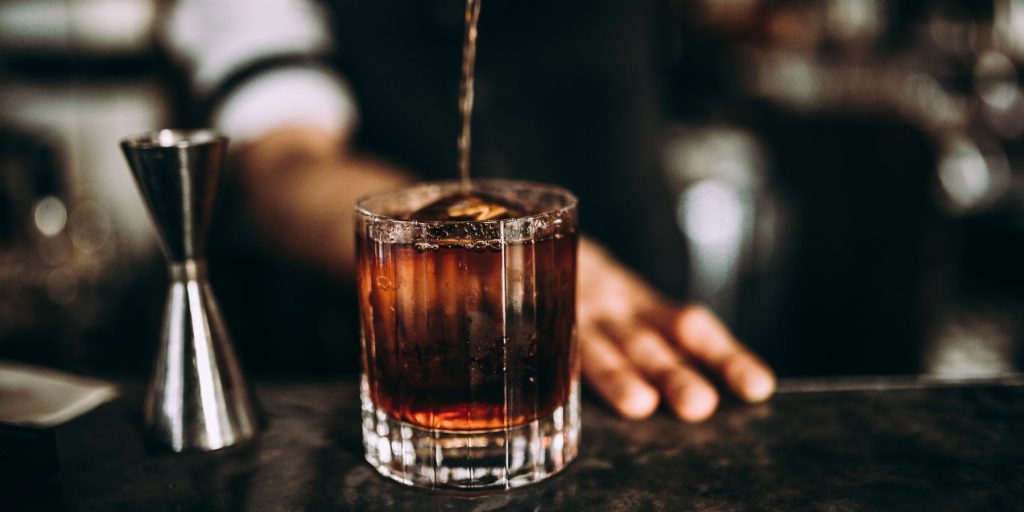A close up shot of a barman pouring bourbon into a rocks glass with ice.