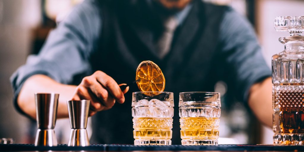 A bartender using a pair of tweezers to drop a dried orange wheel into a tequila Old Fashioned cocktail.