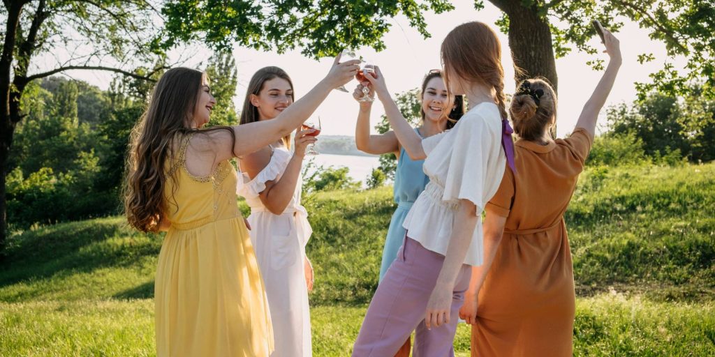 A group of girls having a picnic under trees toasting with cocktails.
