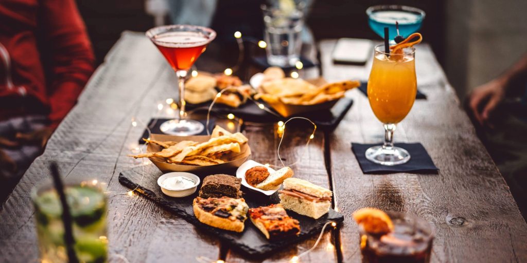 A wooden table with platters of snacks and a selection of cocktails.