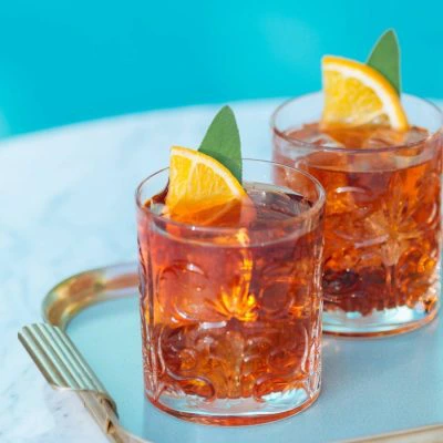 Two Negroni cocktails on a glass tray surrounded by snacks.