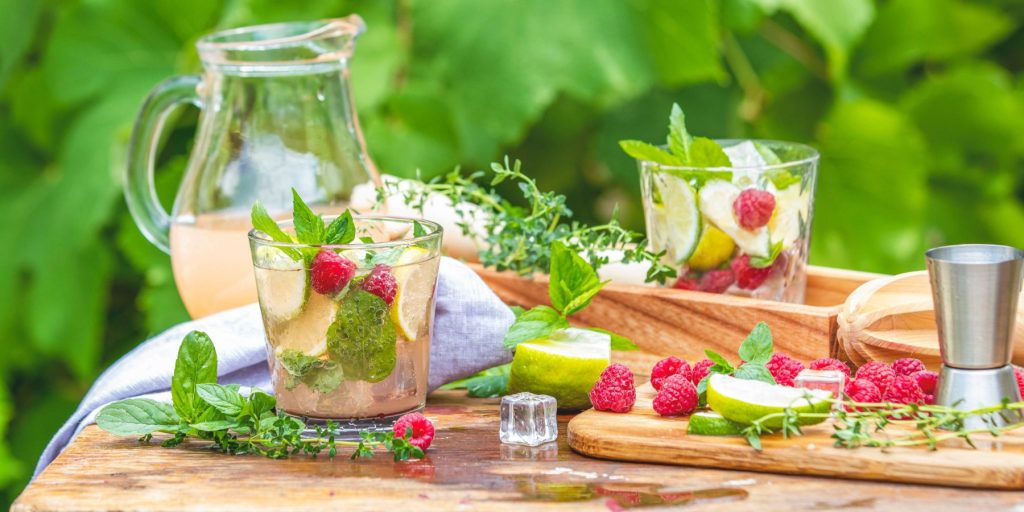 A summer table cocktail set up with a jug of cocktails and several glasses filled with fruity cocktails.