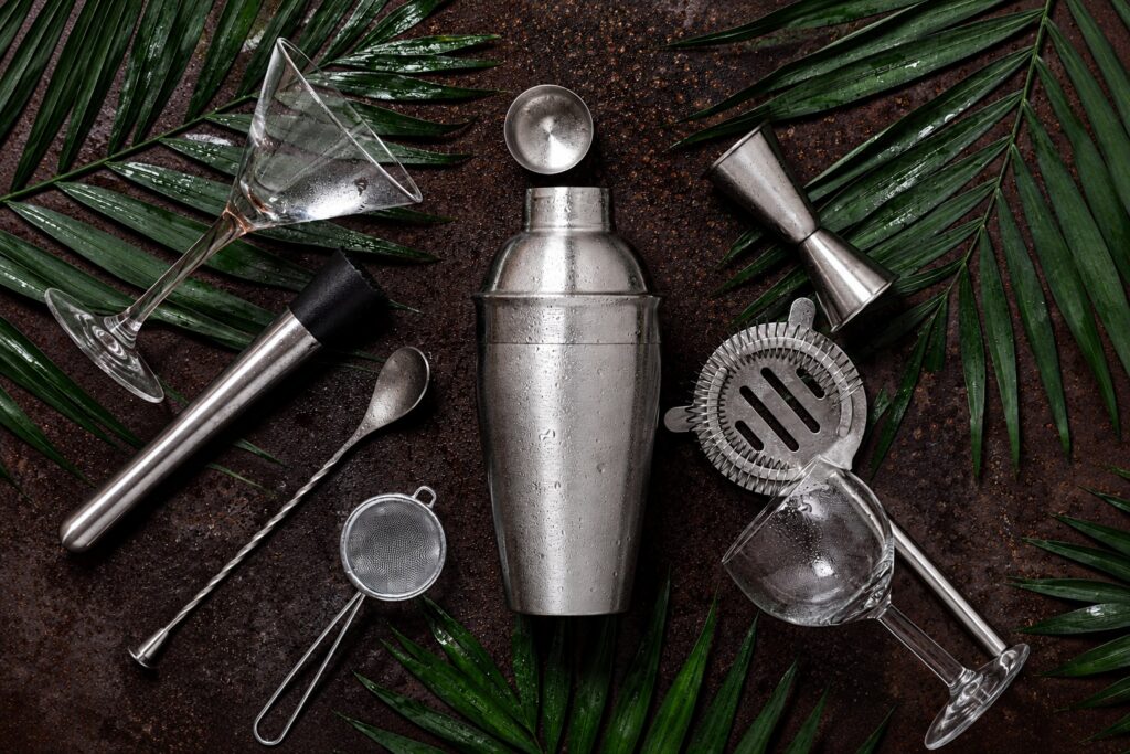 Cocktail-making tools arranged with tropical leaves on a dark surface.