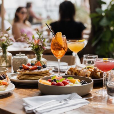 A brunch table with food and cocktails, with blurred people in the background.